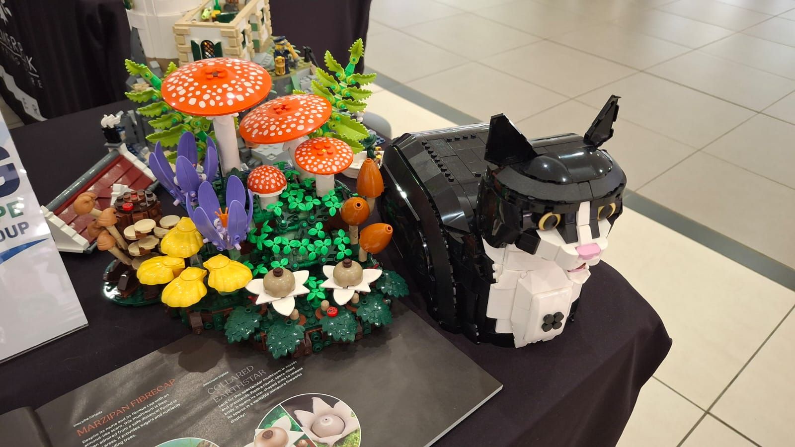 A LEGO mushroom garden next to an original brick-built black and white tuxedo cat